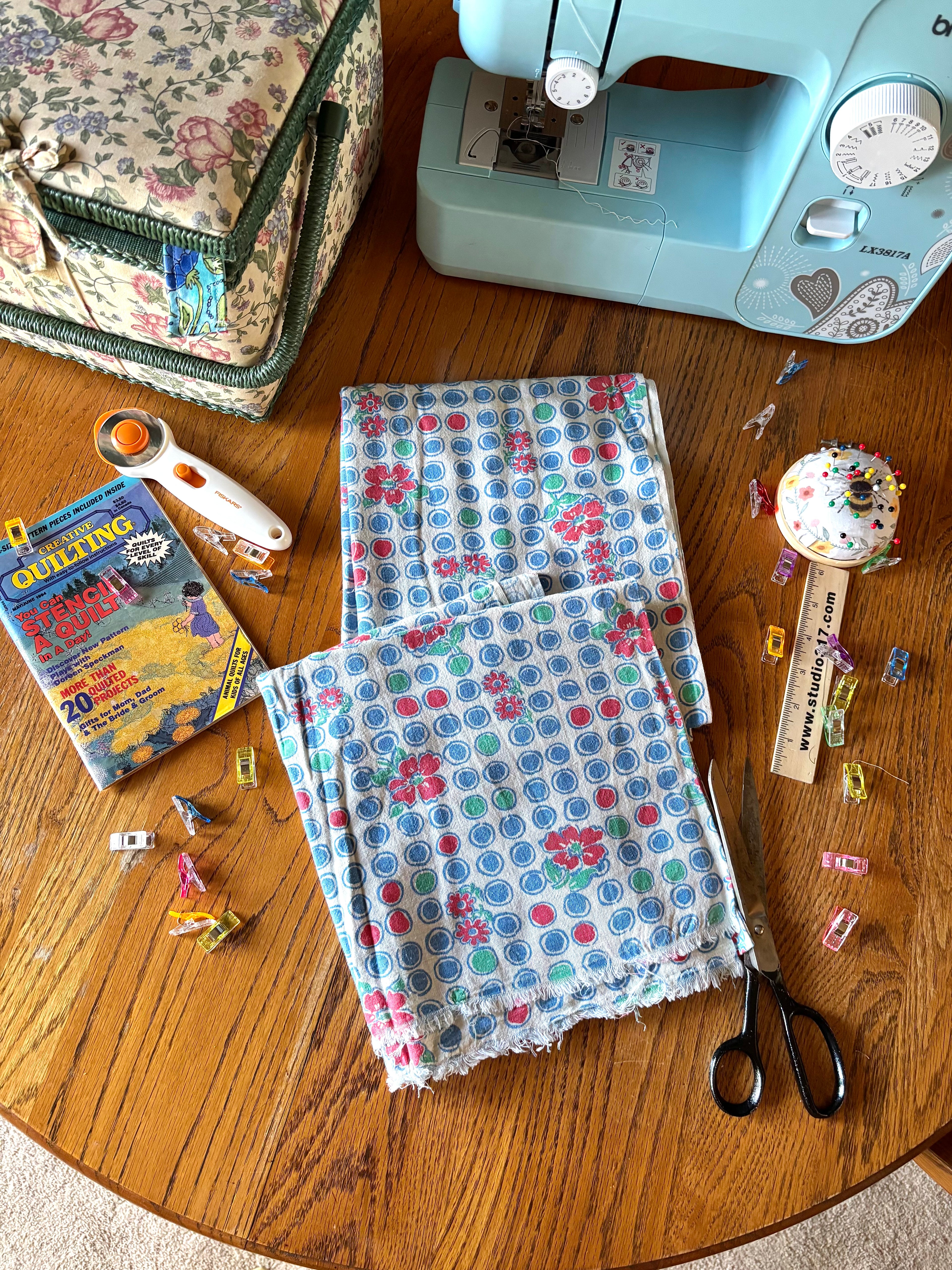 Sewing materials including fabric, scissors, and a sewing machine on a wooden table.